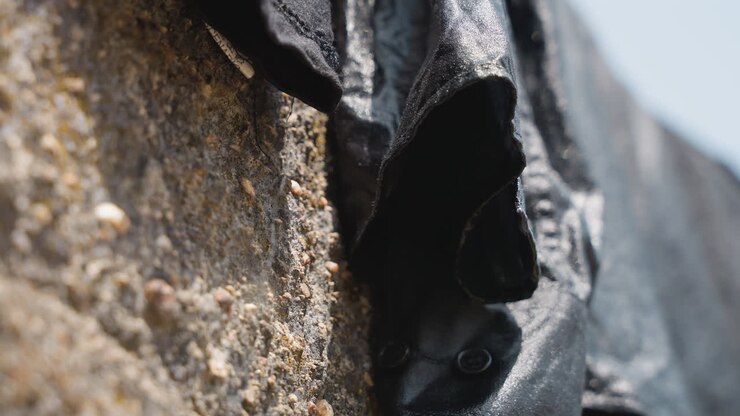 Black garment drying on stone wall crevice, closeup of damp sleeve tucked into rough mortar, gritty pebble detail and weathered texture, domestic laundry chore captured in muted light