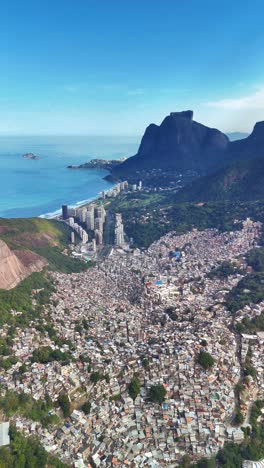 vertical: drone shows favela rocinha with city, blue ocean, and mountains in view - rio de janeiro