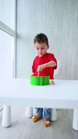 focused baby boy stands at the desk playing with a toy. kid learns colors, shapes and sizes during the game. vertical video.