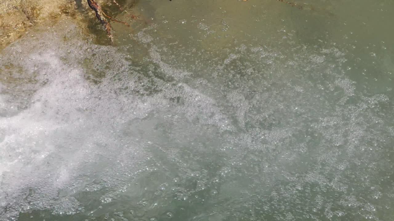 Water splashes down, creating foam bubbles on the surface of a mountain river stream, showcasing the dynamic flow