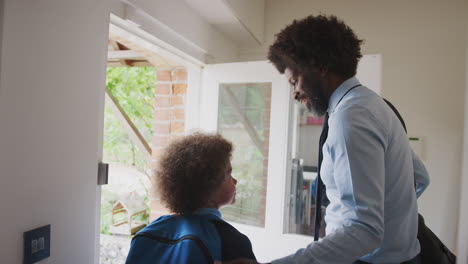 Middle-aged-black-man-dressed-in-a-shirt-and-tie-leaving-home-in-the-morning-with-his-son,-wearing-school-uniform,-seen-from-hallway