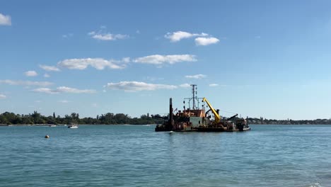 Sarasota,-Florida---December-19,-2020:-A-dredger-sitting-in-the-clear-blue-water-of-an-inlet-from-the-Gulf-of-Mexico