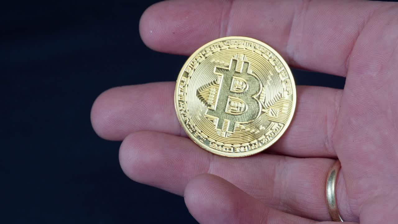 moneda de bitcoin sostenida en la mano, reflejando la luz contra un fondo oscuro, simbolizando la criptomoneda y la riqueza