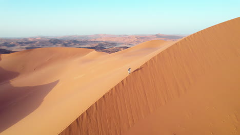 Tiro-De-Drone-De-Hombre-Caminando-En-Dunas-De-Arena-Del-Desierto-Del-Sahara-En-Argelia