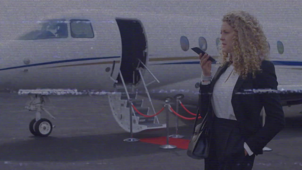 Donna d'affari che solleva lo smartphone e fa una chiamata sul tappeto rosso, mostrando un glitch su un jet.