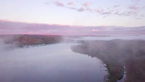 aerial sunrise wide shot flying through cloud fog to reveal misty lakes and pink clouds and fall forest colors in kawarthas ontario canada