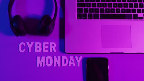 composition of laptop, headphones and smartphone with cyber monday text on purple background