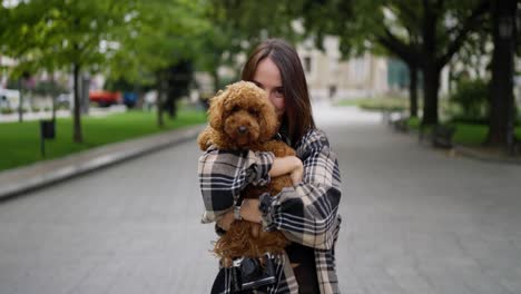 mujer feliz sosteniendo a su adorable perro caniche en el parque