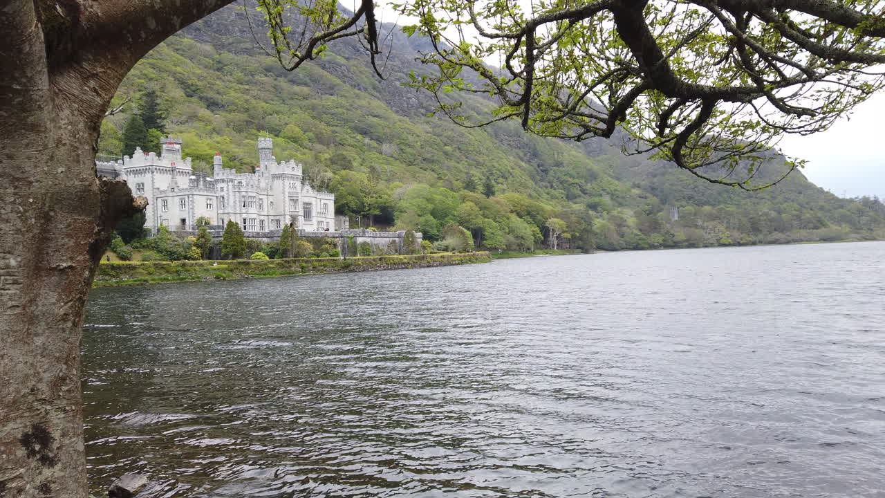 Scenic landscape capturing historic Kylemore Abbey nestled among green mountains, reflecting perfectly on calm lake waters