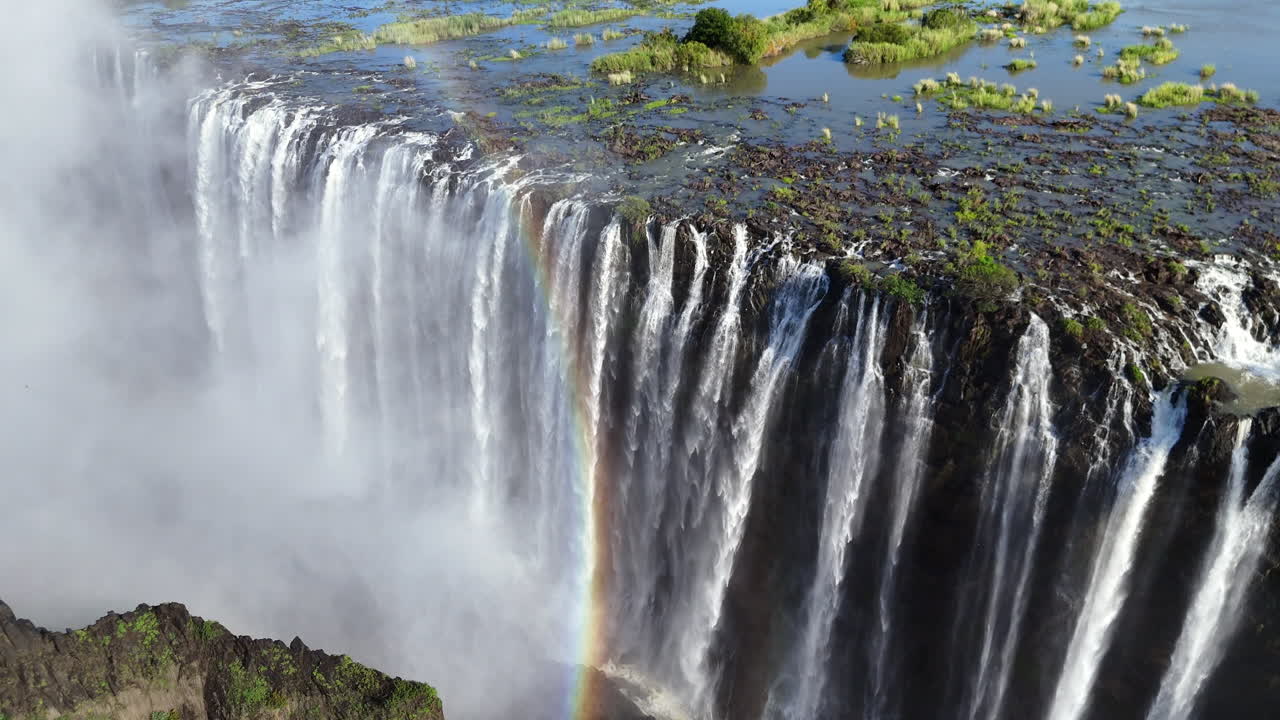 Aerial view of Victoria Falls with powerful waterfall plunging into gorge, mist rising above lush green forest, dramatic natural wonder and iconic travel destination in Africa