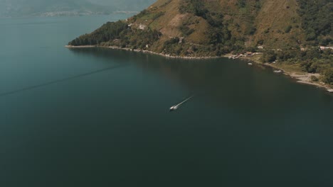 Drone-aerial-shot-of-a-boat-driving-over-lake-Atitlan,-Leaving-San-Marcos-Dock-in-Guatemala