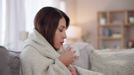 woman wrapped in a blanket on a couch, drinking a cup of tea