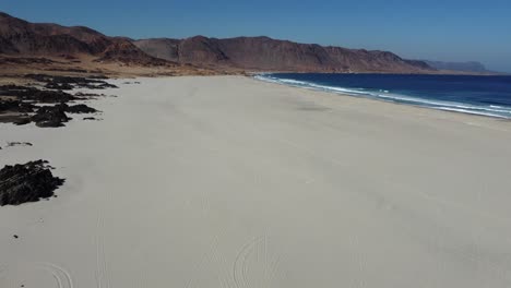 aerial tilts from rugged rocks to expansive atacama sandy ocean beach