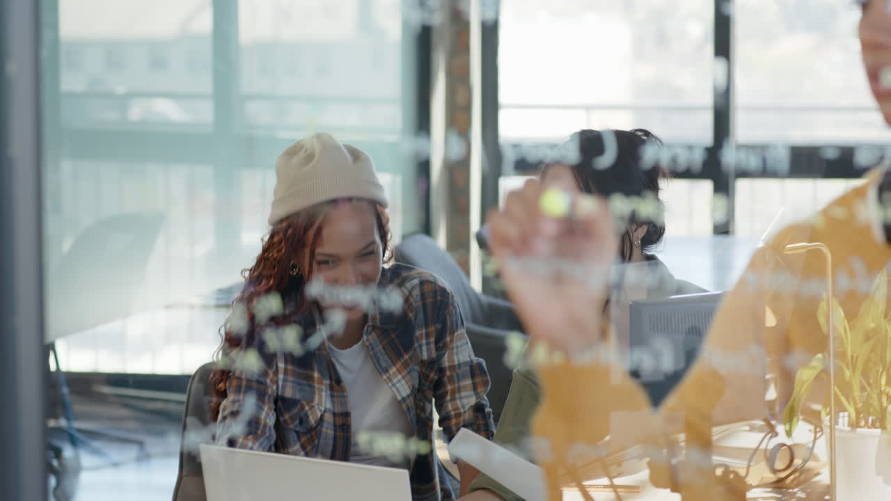Diverse female team collaborating on coding project, writing on glass board in modern office
