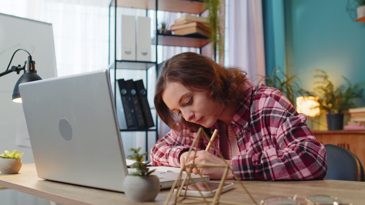 Business woman working on laptop computer online writing notes in planner notebook at office