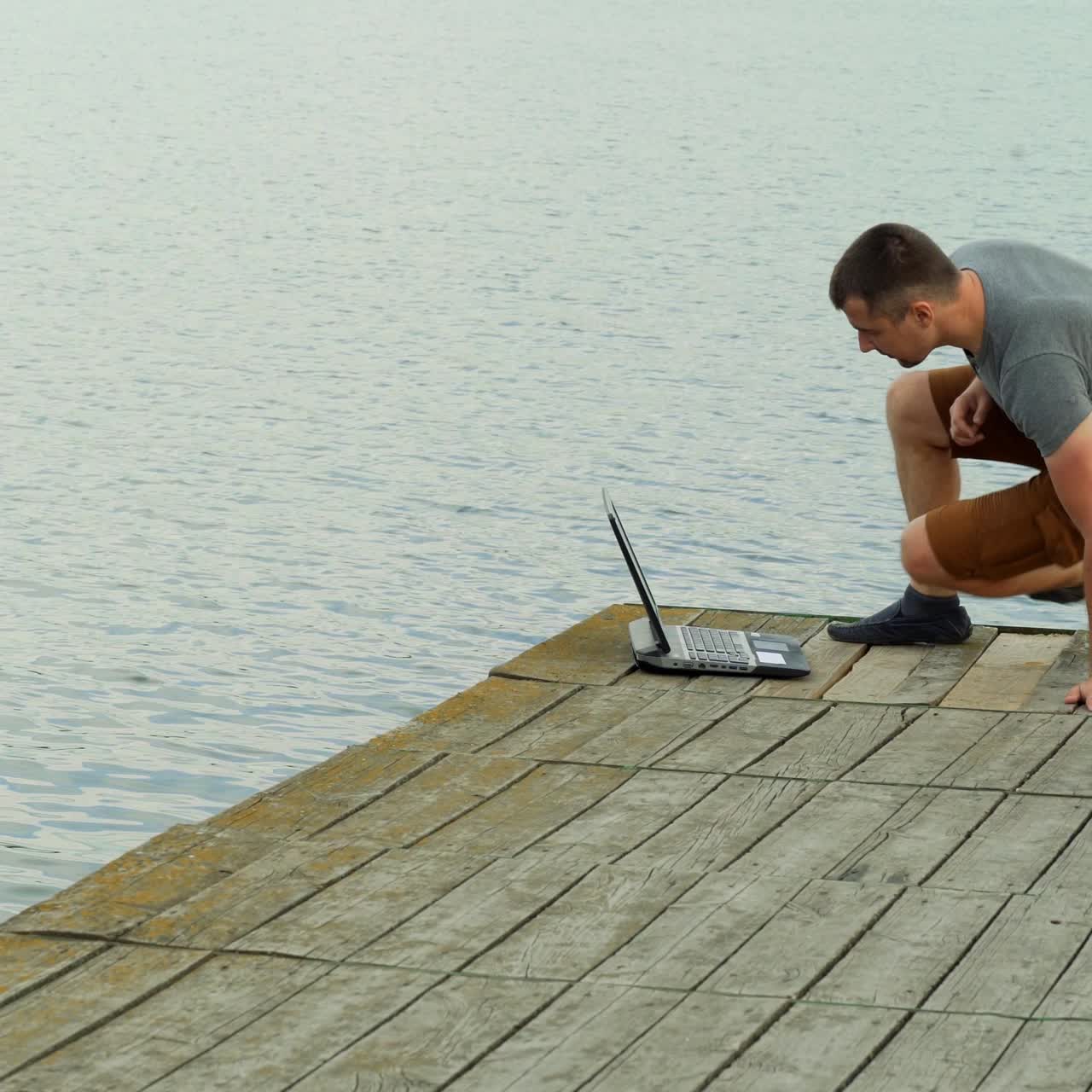 Young man working on laptop while sitting ?n old pier