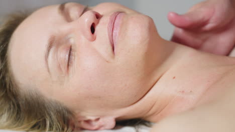 recipient smiles eyes closed expressing deep relaxation as beauty technician glides fingertips from side of neck to shoulder applying gentle pressure in spa environment during serene massage session