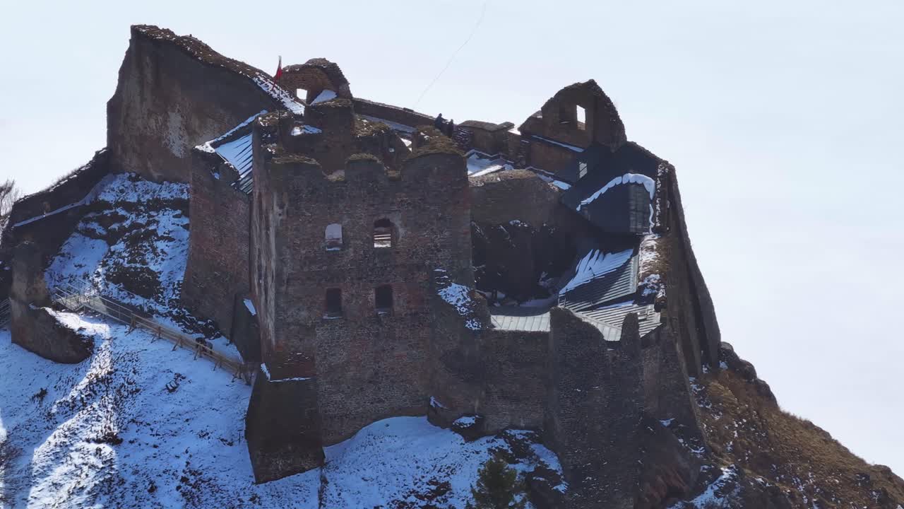 Luftfoto af historiske slotsruiner omgivet af sne i vinterlandskab.