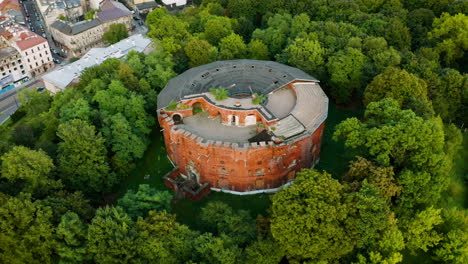 Aerial-view-of-alone,-rounded,-brick-fortress-in-forest-in-Krakow,-Poland