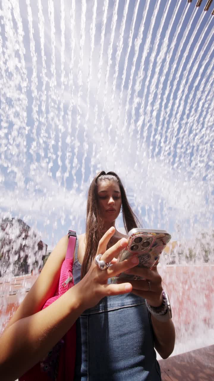 Young Woman Using Phone Under a Water Fountain