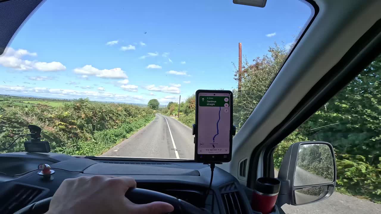 Driver's perspective of a sunny country road with GPS navigation, clear blue sky