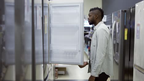 Un-Hombre-Inspecciona-El-Diseño-Y-La-Calidad-Del-Refrigerador-Antes-De-Comprarlo-En-Una-Tienda-De-Electrónica-De-Consumo