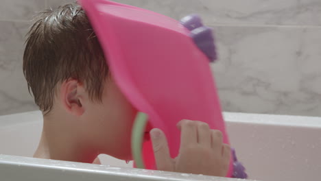 imaginative child using toy bathtub as helmet playing in the bath