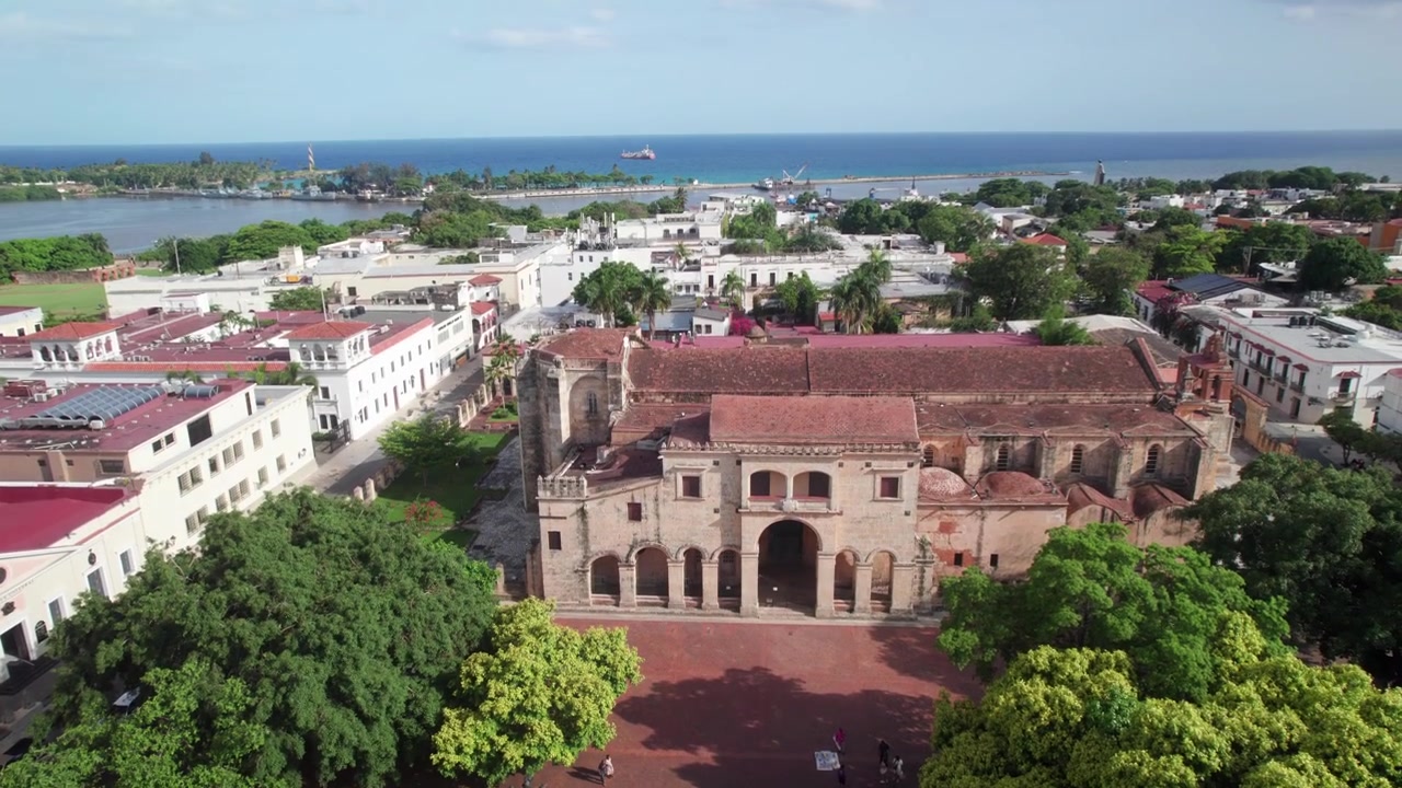 Ripresa aerea da drone ad alta angolazione che cattura la storica Cattedrale di Santo Domingo e il Parque Colón, evidenziando l'architettura coloniale, il verde del parco e la disposizione urbana.