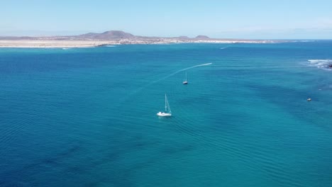 High-aerial-view-of-sail-boats-on-the-surface-of-beautiful-blue-coastal-waters-with-an-island-on-the-horizon