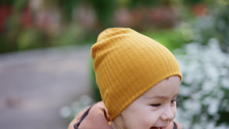 happy caucasian toddler in cap and jacket running outdoors. beautiful flowers at backdrop in the park.