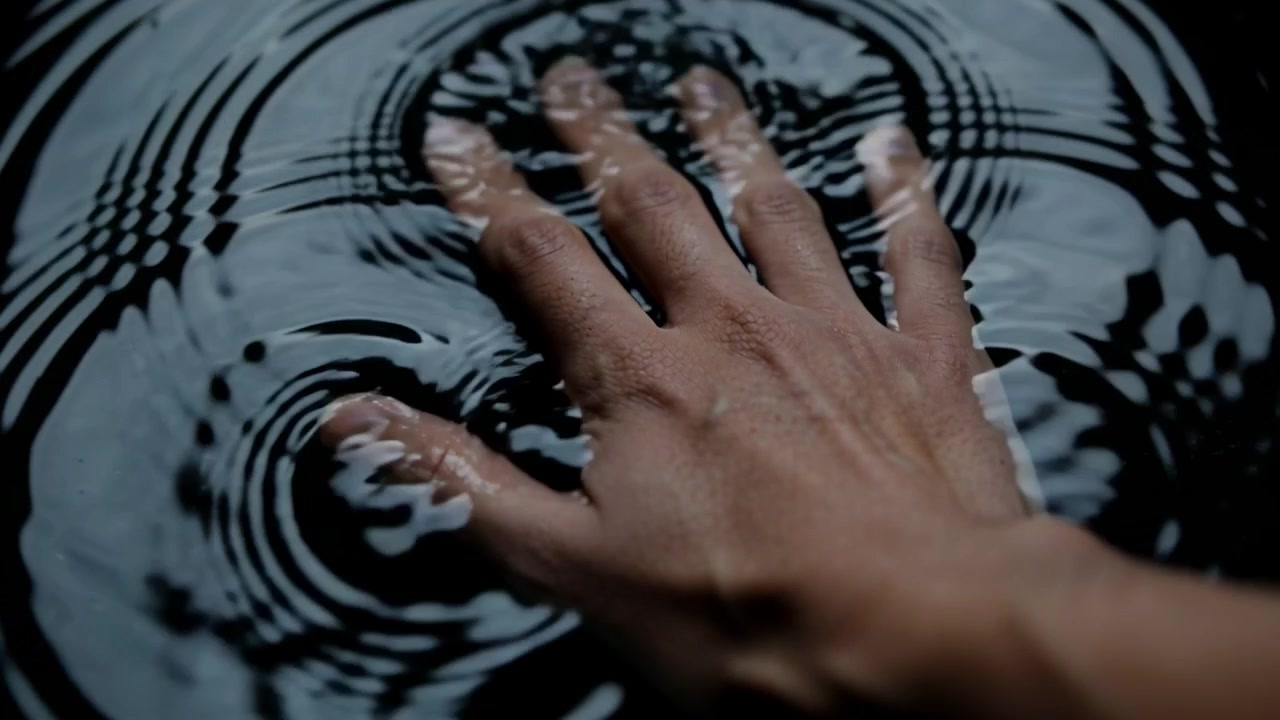 Moving right hand touching dark water, pressing and sliding to create circular ripple patterns
