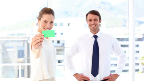 businessman giving card to businesswoman who shows it to camera