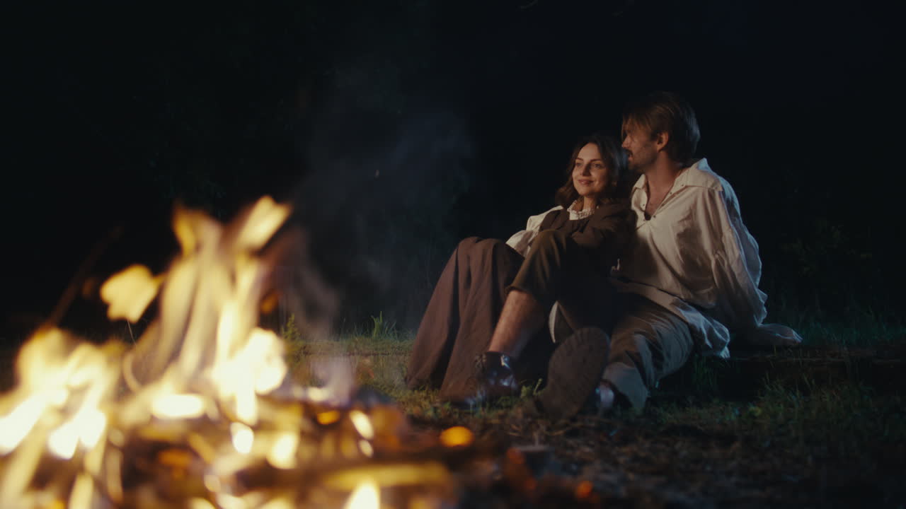 Couple sitting by a campfire at night