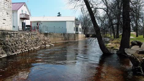 Luftdrohnen-Speditionsaufnahme-über-Einem-Wasserkanal-Im-Dorf-Mishicot-Town,-Manitowoc-County,-Ost-Zentral-Wisconsin,-USA-Mit-Trockenwald-Auf-Der-Einen-Seite-Und-Wohnhäusern-Auf-Der-Anderen-Seite