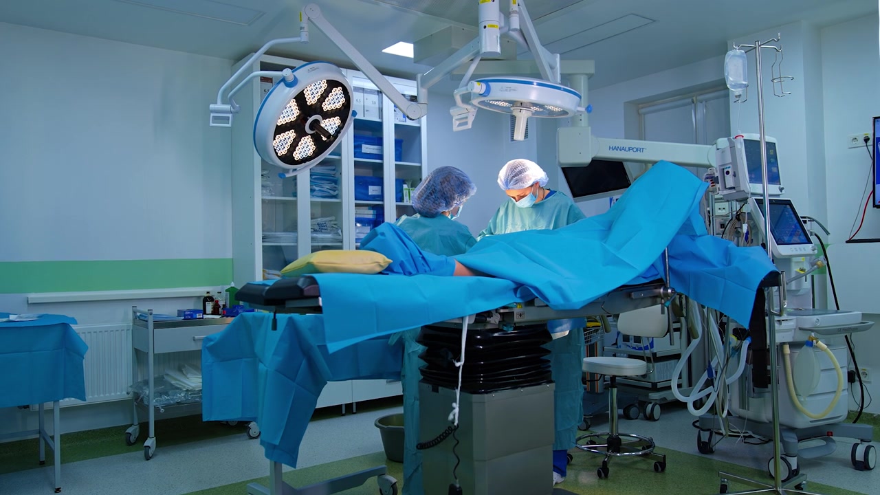 Advanced surgery room with modern medical equipment. Female surgeon and scrub nurse work at operating table.