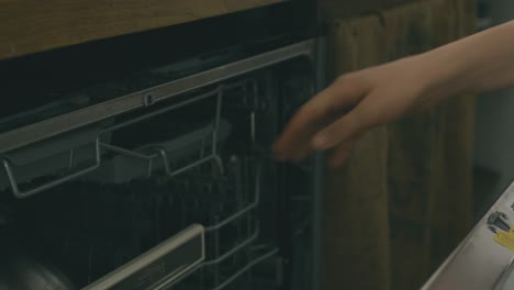 detalle de dos manos abriendo un lavavajillas, insertando un recipiente y lavando