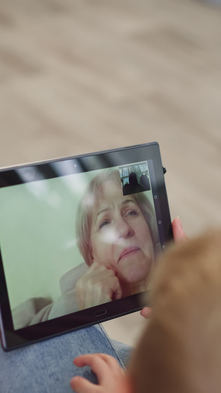 mamá y los niños hablan con la abuela en video llamada a través de una tableta moderna sentada en casa. pantalla de un dispositivo electrónico en un fondo borroso de primer plano
