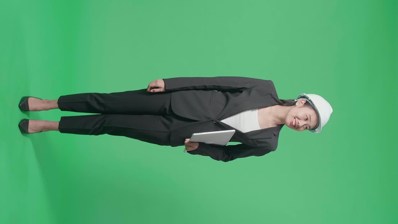 Full Body Of Smiling Asian Female Engineer With Laptop Looking Around And Shaking Her Head In The Green Screen Studio