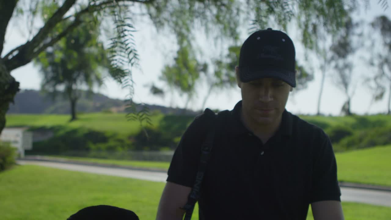 Primo piano di un golfista che cammina lungo un campo da golf verso la telecamera.