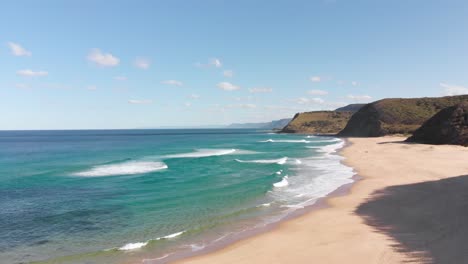 Drone-view-of-waves-crashing-onto-a-beach-surrounded-by-high-cliffs-and-mountains-in-Australia