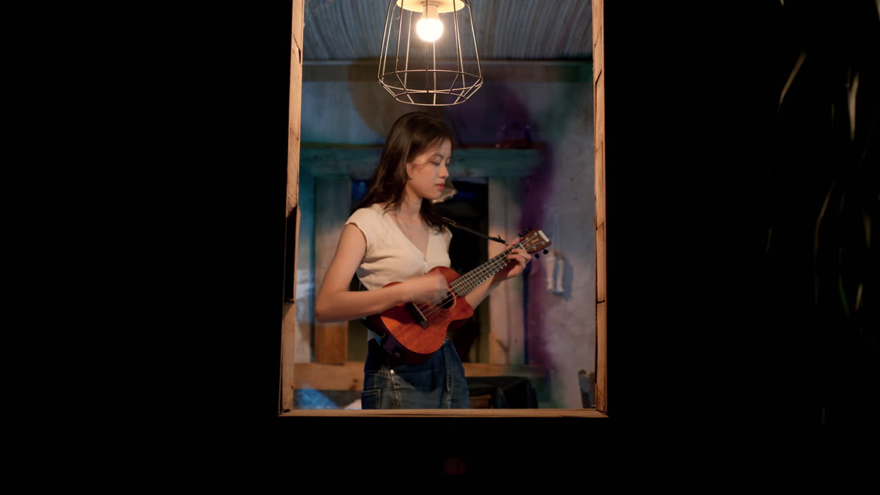 chica asiática tocando el ukulele en la ventana, estática