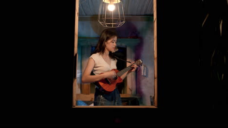 Asian-girl-playing-ukulele-at-the-window,-static