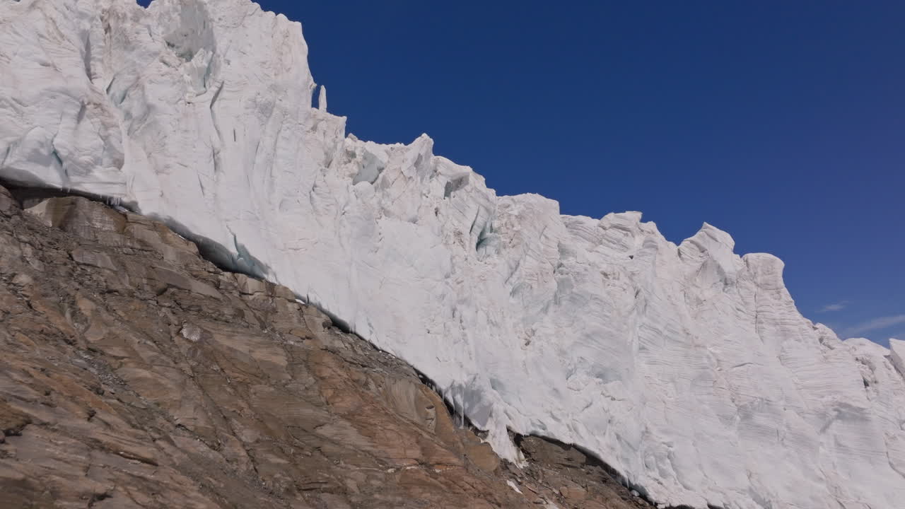 A powerful drone shot revealing massive overhanging seracs and towering ice cliffs in Saas-Fee, Switzerland. The frozen formations glisten under alpine light, showcasing the raw power of the glacier