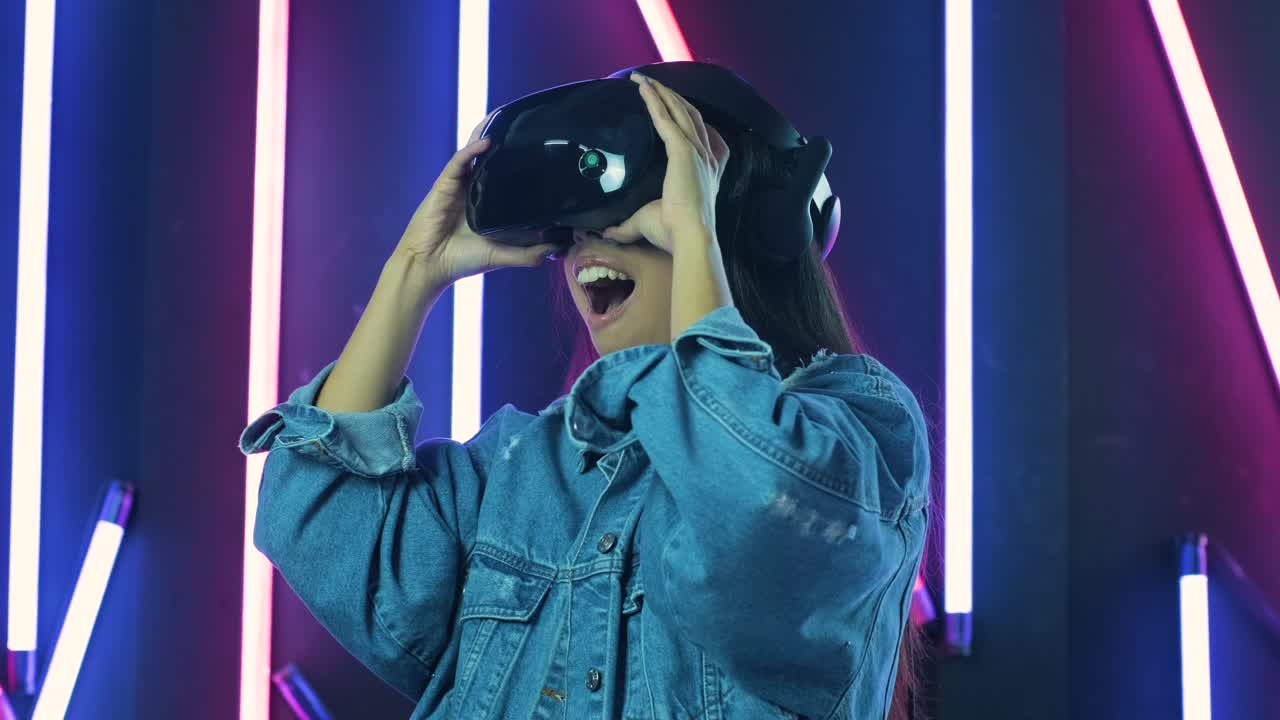 una giovane donna si mette le cuffie vr e si chiede come sia fantastico nel mondo vr. casco di realtà virtuale su sfondo di illuminazione a colori