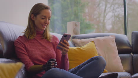 woman with prosthetic arm on sofa at home using mobile phone