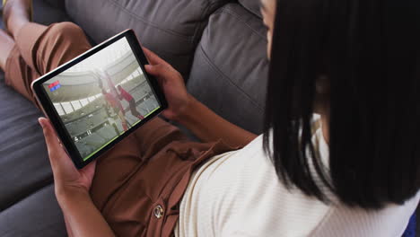 compuesto de una mujer sentada en casa en el sofá viendo un partido de rugby en la tableta