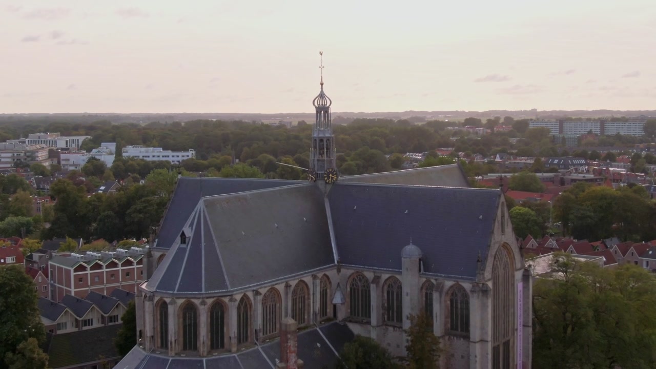 Push forward and rise past an ornate tower over leafy Alkmaar, warm cloudy dusk.