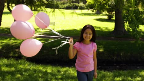 little girl carrying balloons for breast cancer awareness in the park