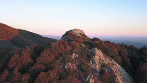 zoom out drone shot of a woman doing yoga on top of a mountain with the first lights of sunrise