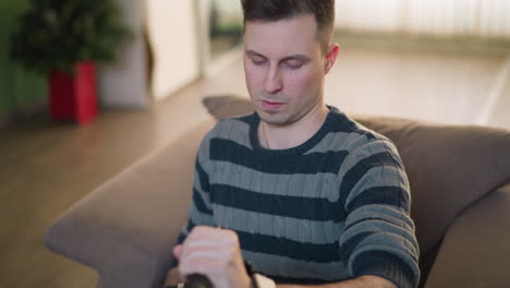man focused on adjusting video camera with microphone, sitting on couch in living room. modern setup with soft natural light, preparing for filming or content creation in a creative space